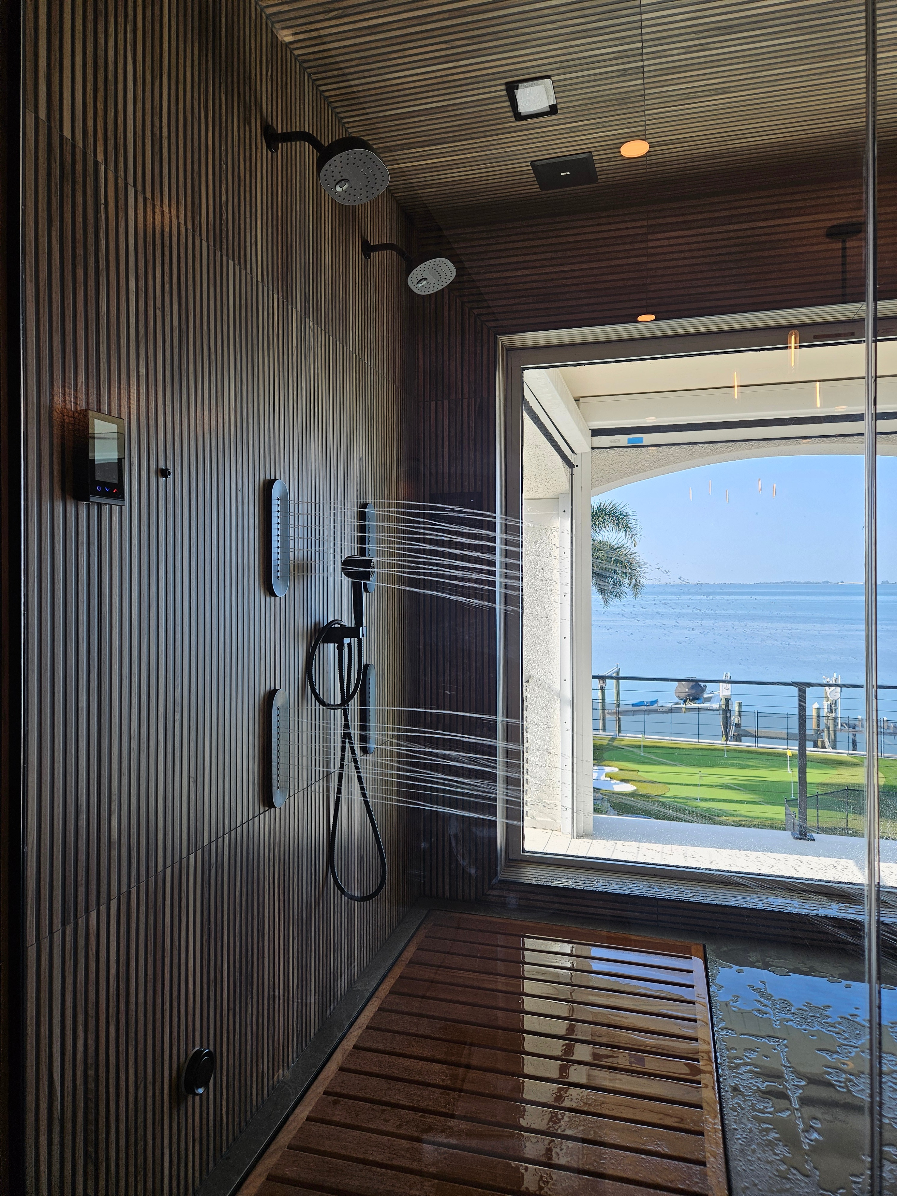 Finished luxury spa shower with dark wood-slat walls, multiple shower jets, and a bay view window by Grout & About